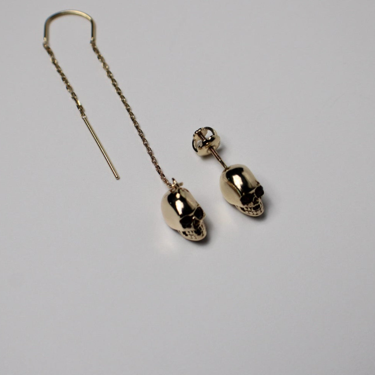 Gold skull-shaped earrings on a light gray background