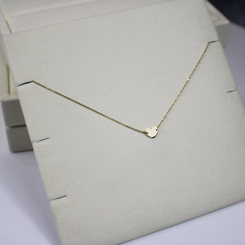 Gold necklace with a heart pendant on a light gray surface