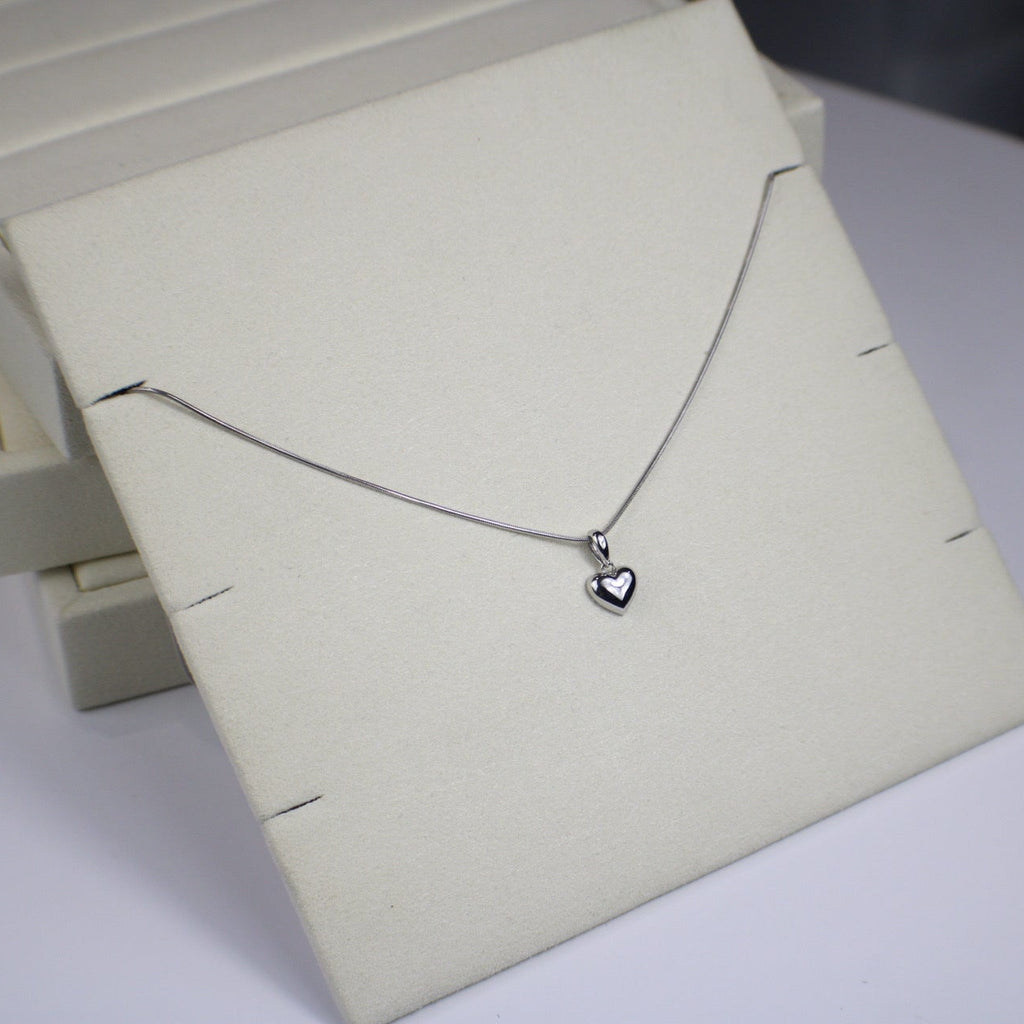 Silver necklace with a heart pendant on a white stand