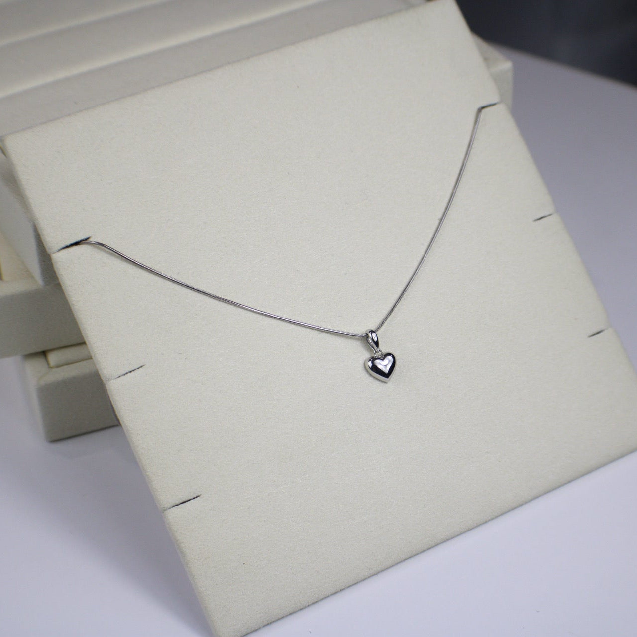 Silver necklace with a heart pendant on a white stand