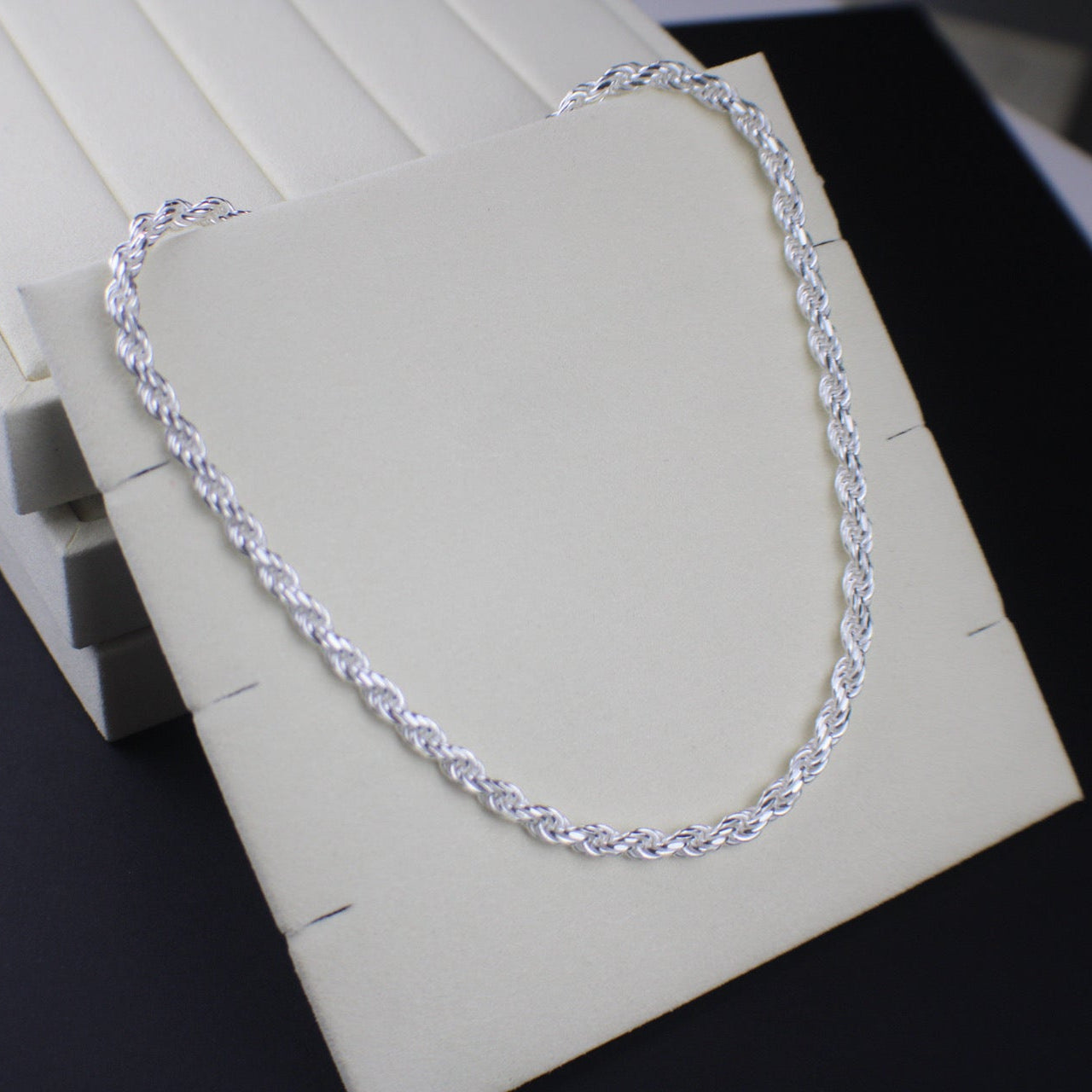 Silver chain necklace on a white stand with a dark background