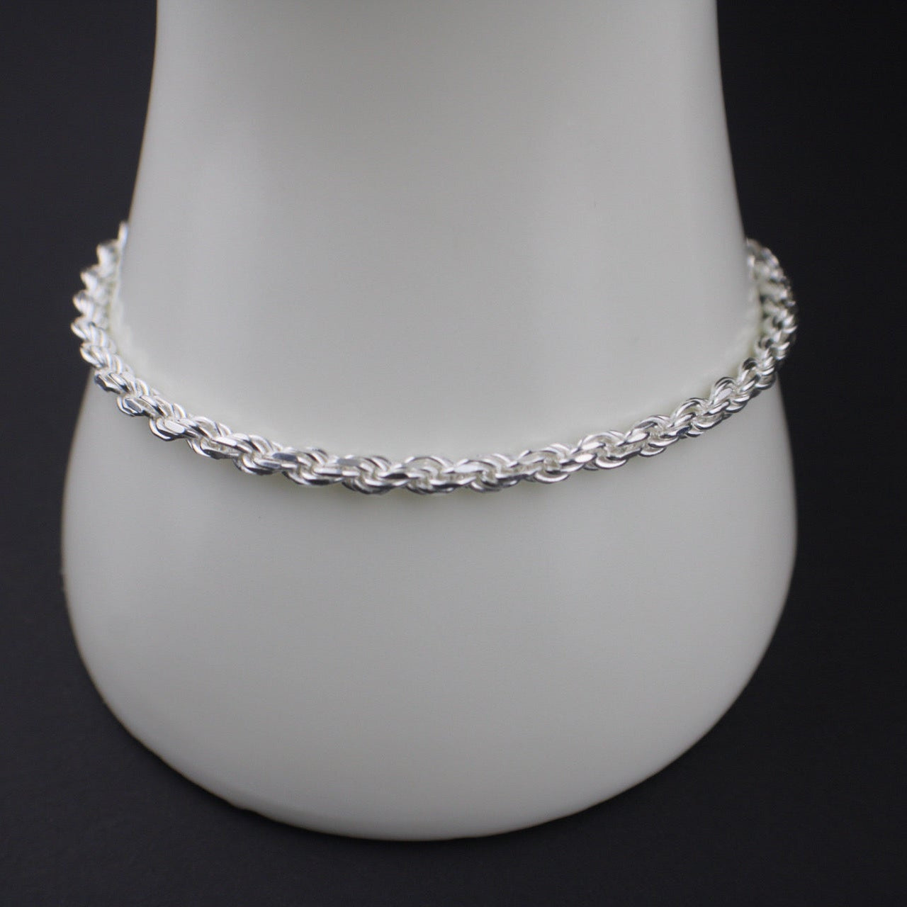 Silver bracelet on a white mannequin arm against a black background