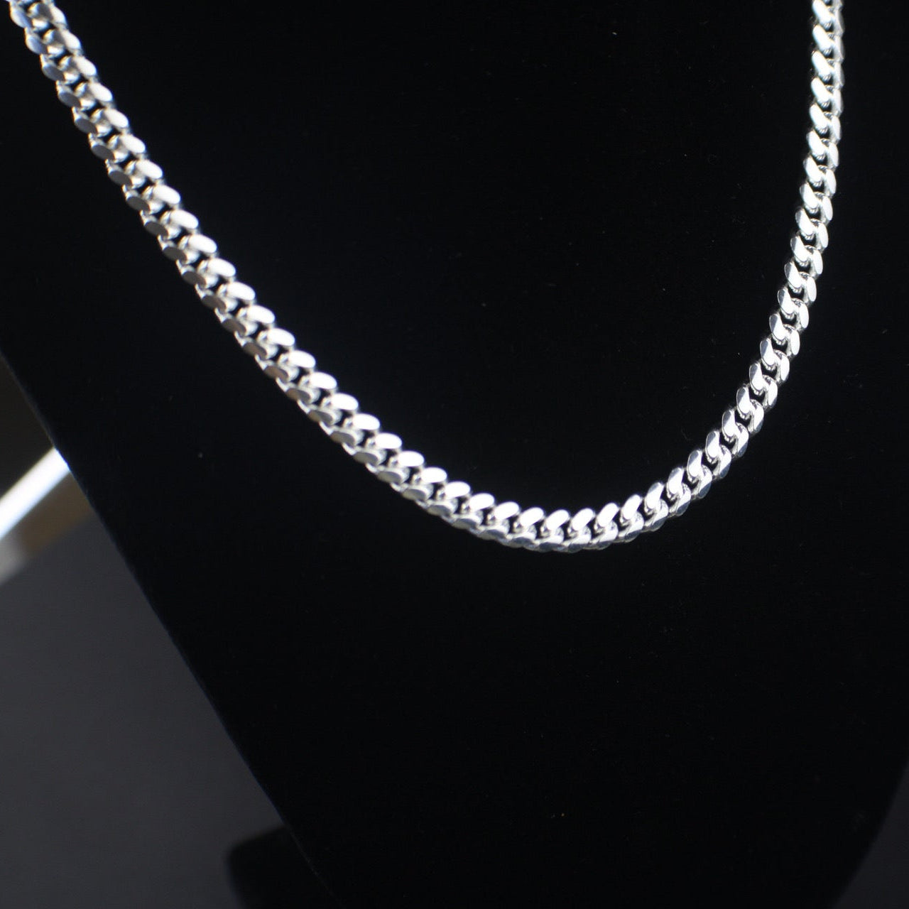 Silver chain necklace on a black stand with a blurred background