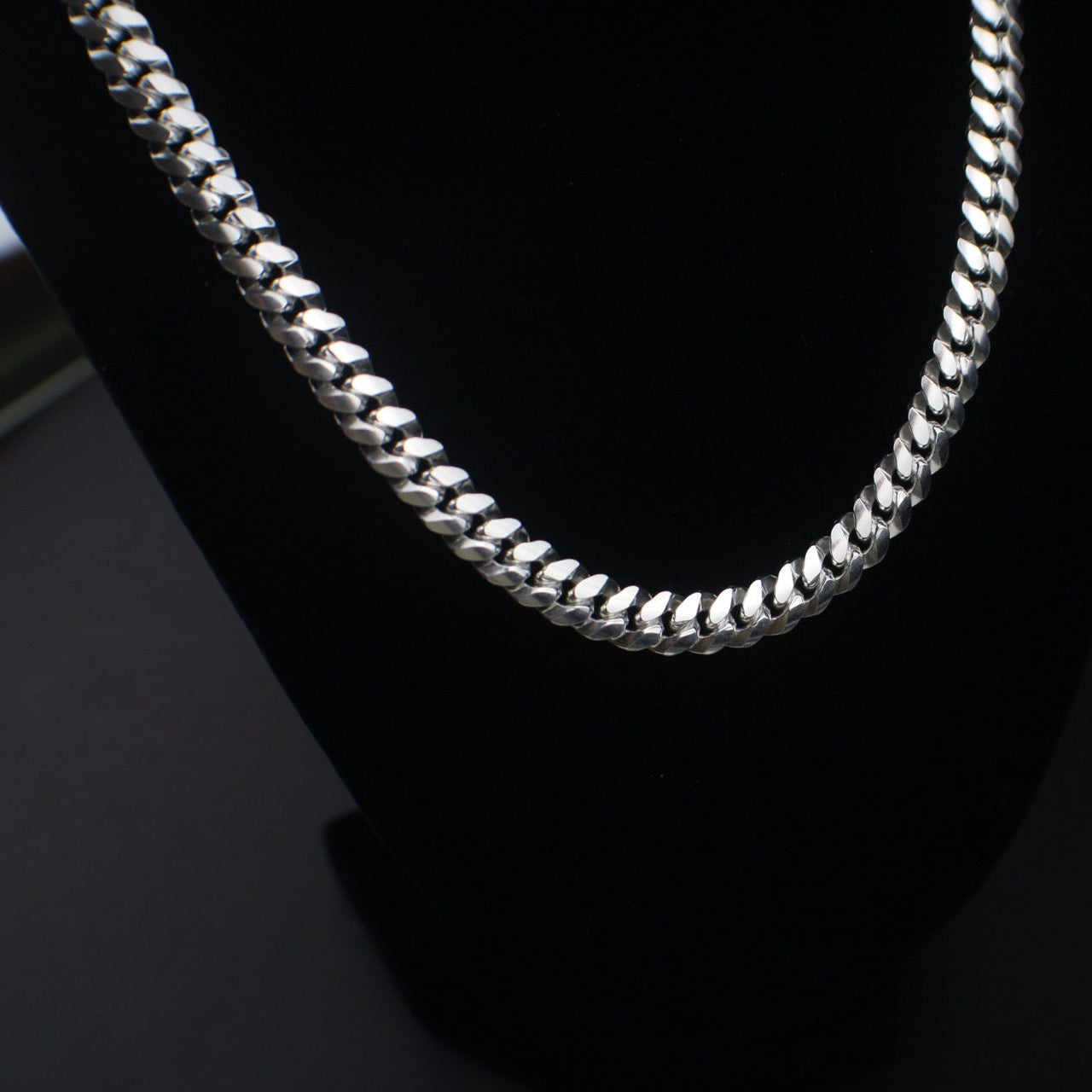 Silver chain necklace on a black stand with a dark background