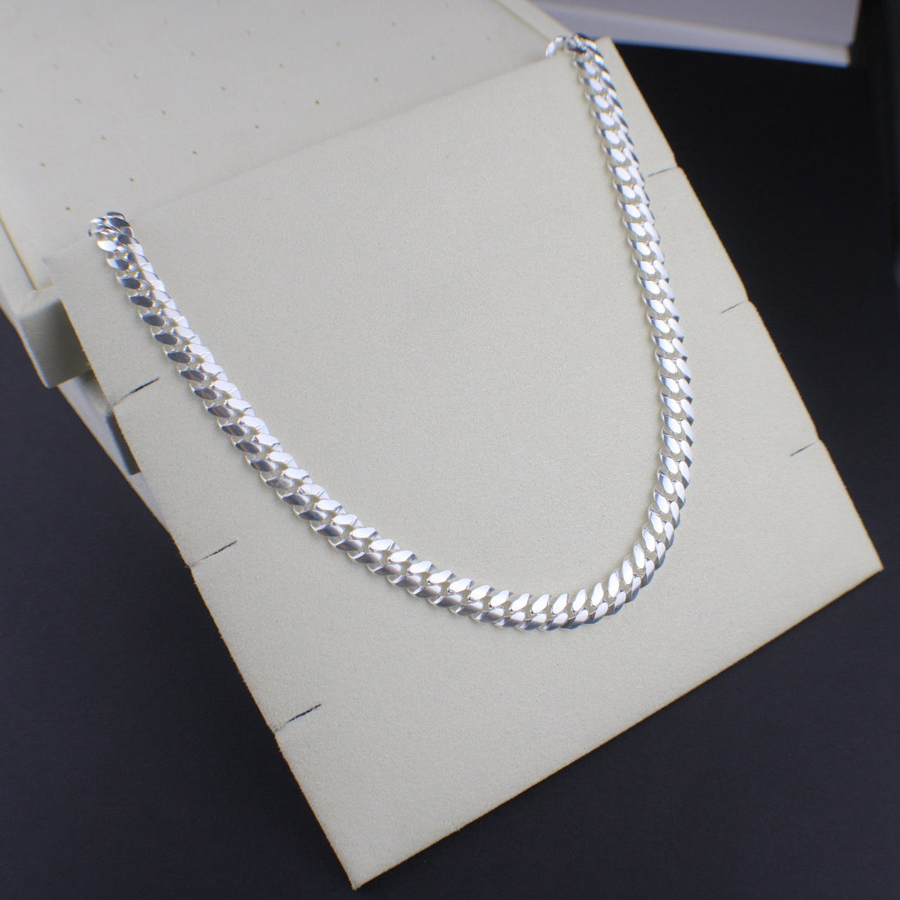 Silver chain necklace on a white box with a dark background