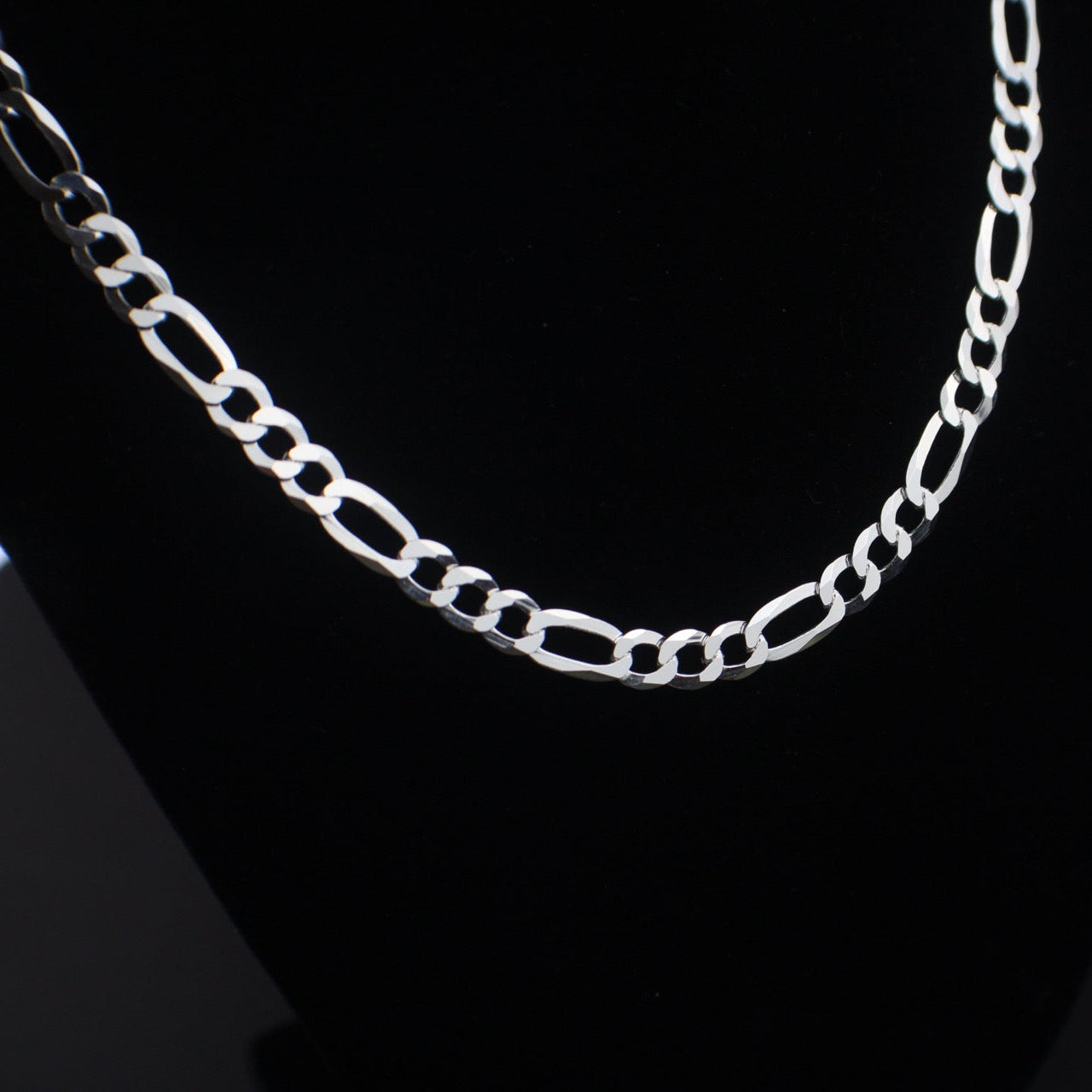 Silver chain necklace on a black stand with a dark background