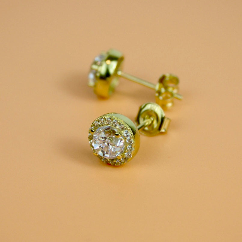 Gold earrings with clear gemstones on a beige background